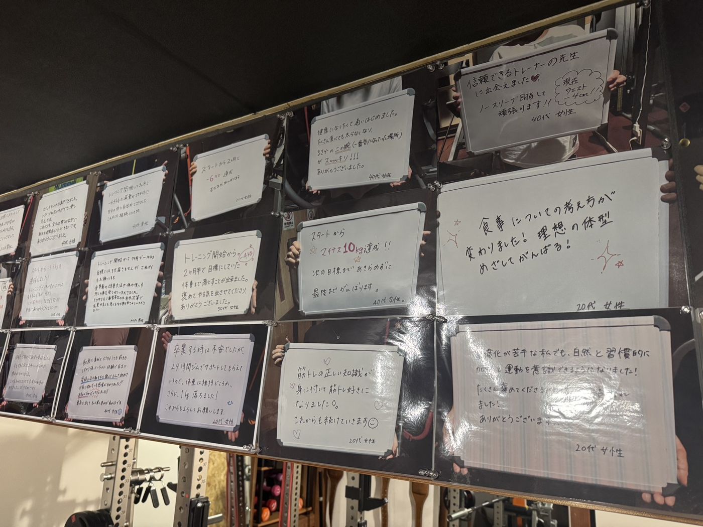 お客様が手書きのホワイトボードを持った写真が壁一面に並んでいる